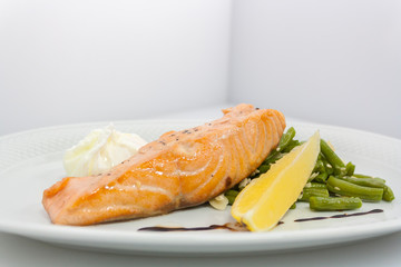salmon steak with poached egg, beans, sesame and lemon on a white plate
