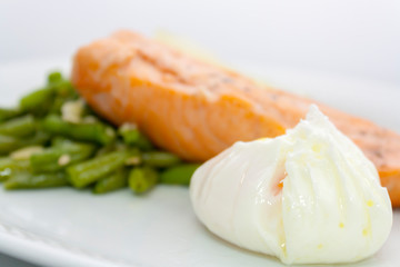poached egg on the background of salmon steak, beans, sesame and lemon on a white plate