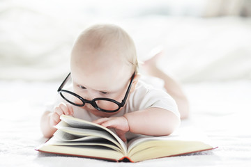 A newborn baby is lying on a soft bed in glasses.