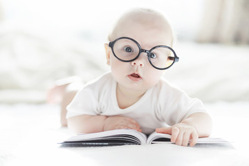 A newborn baby is lying on a soft bed in glasses.