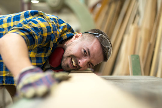 Close up of smiling carpenter worker checking quality and smoothness of wood product in carpentry workshop.