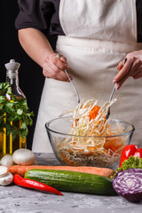 a young woman in a gray apron mixes a salad of cabbage