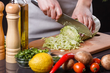 A young woman in a gray apron cuts chinese cabbage