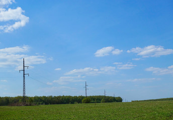 Fototapeta na wymiar Green field with electric pillars against the blue sky, Russia