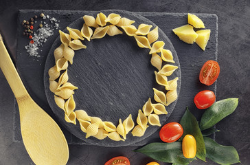 Pasta shells on black stone. Tomatoes and bay leaves with allspice and sea salt.