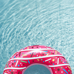 Inflatable float rubber ring in the form of a pink donut in the blue water of the pool.