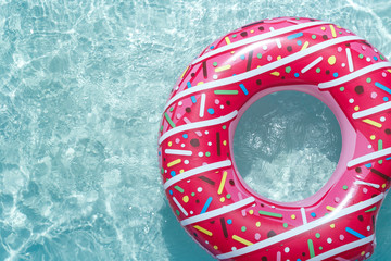 Inflatable float rubber ring in the form of a pink donut in the blue water of the pool.