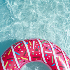Inflatable float rubber ring in the form of a pink donut in the blue water of the pool.