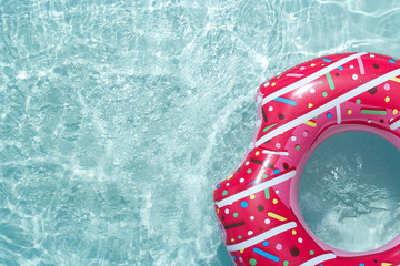 Inflatable float rubber ring in the form of a pink donut in the blue water of the pool.