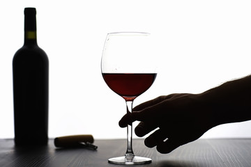 A glass of red dry wine on the table. Dark bottle and glass of wine.