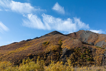 Triangluar shaped ridge line is covered in  dark rock covered with browns and golds of an Alaskan fall