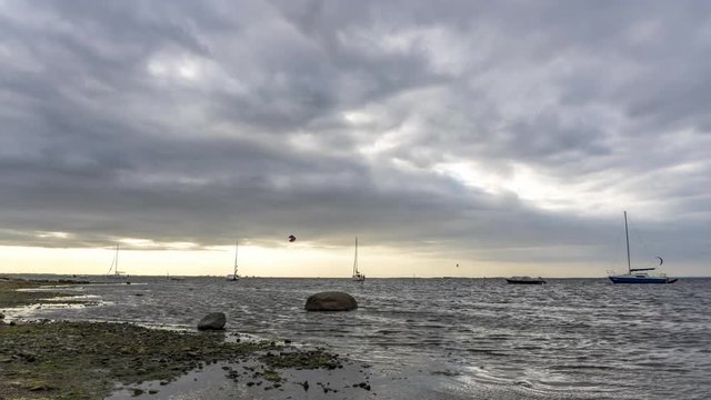 landscape time lapse of the sea with kitesurfers, sailing boats and beatiful clouds near sunset