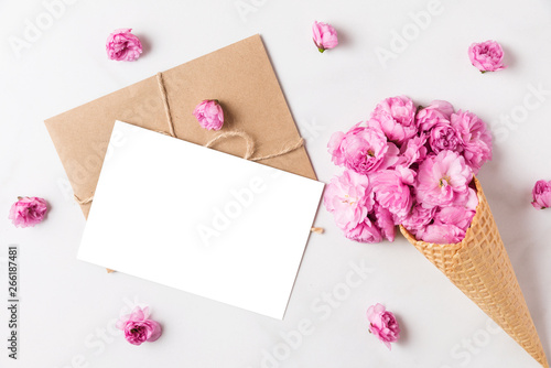 blank greeting card and ice cream cone of pink blossom cherry flowers in waffle cone on marble background. flat lay