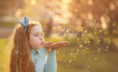 Little girl blowing gold confetti with her hand.