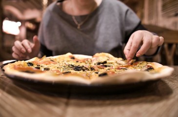 Girl sitting in a cafe takes a slice of pizza, close-up