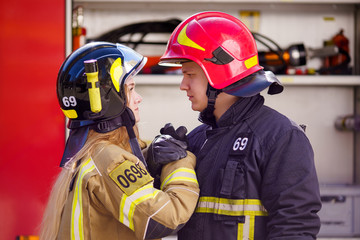 Side view of girl firefighter and man wearing helmets doing handshake near fire engine