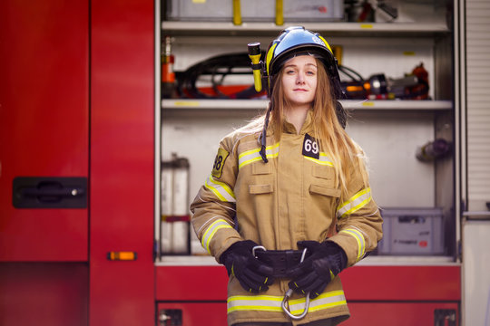 Image of blonde firefighter in helmet standing near fire truck at fire station