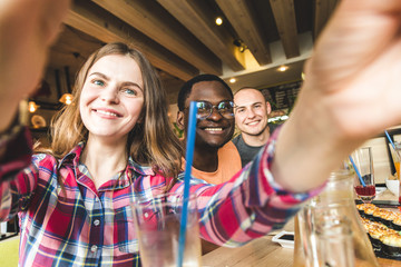 Group of young cheerful friends are sitting in a cafe, eating, drinking drinks. Friends take selfies and take pictures.