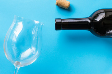 Dark bottle of wine, empty wine glass and cork on a blue background.