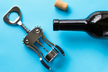A corkscrew, a cork and a dark bottle of wine against a blue background.