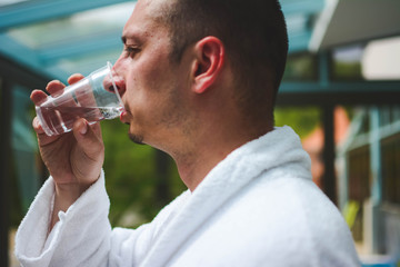 A man enjoys drinking pure spring cold / hot water from a plastic glass. Relax in the spa wellness...