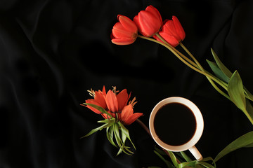 A cup of coffee and a tulip on a black background close-up, selective focus. The elegant design of your evening