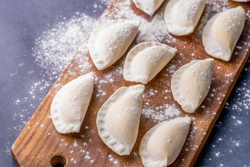 Fototapeta na wymiar Frozen dumplings on a cutting board. Ingredients and flour around on background.