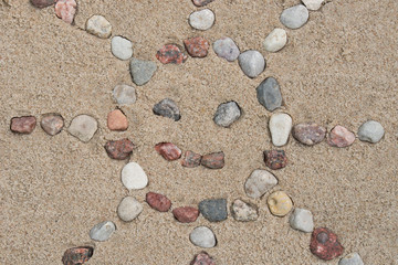 Fototapeta na wymiar sun shape made of pebble stones on sand background