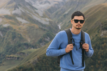 Fototapeta premium Young tourist man with a backpack against the background of the Caucasus Mountains, Georgia on a foggy day