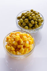 canned corn and green peas in a glass bowl on a white background