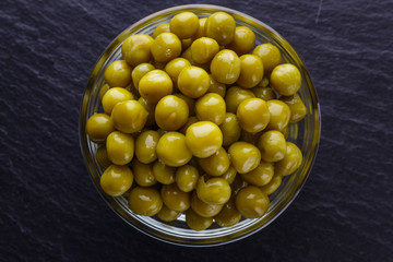canned green peas in a glass bowl on a dark stone background