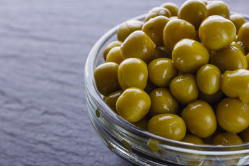canned green peas in a glass bowl on a dark stone background