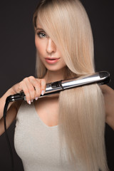 Beautiful blond girl with a perfectly smooth hair, classic make-up with curling styler in the hands.