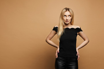 Young beautiful woman with slim perfect body and with blonde hair in black leather pants and in a black blouse at the orange background, isolated