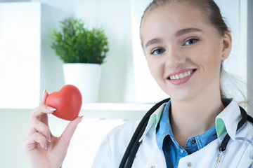 Beautiful Caucasian smiling female doctor hold in arms red toy heart closeup. Cardio therapeutist student education CPR 911 life save. Physician make cardiac physical pulse rate measure arrhythmia