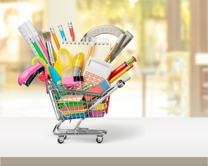 Variety office supplies in little shopping cart on wooden table  on background