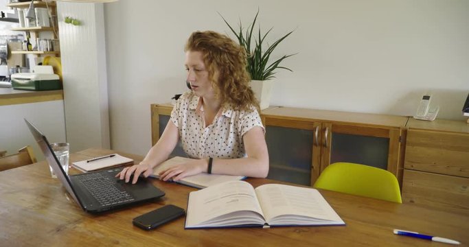 Young studen, blonde woman studying and working behind laptop, with books and notepad