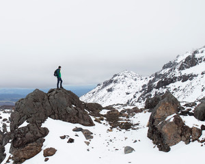 Man standing on a rock on a mountain looking out over a snow covered landscape