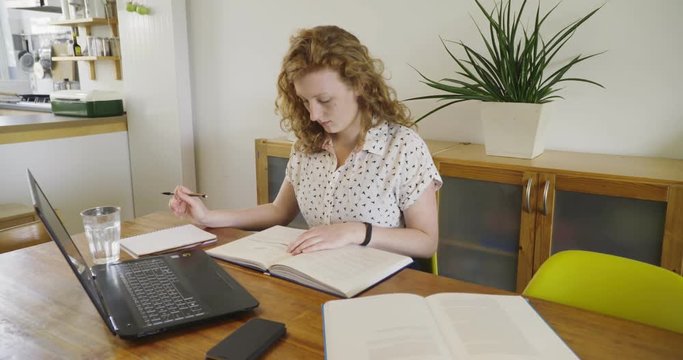 Young studen, blonde woman studying and working behind laptop, with books and notepad