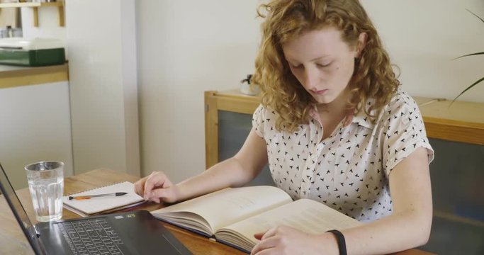 Young studen, blonde woman studying and working behind laptop, with books and notepad