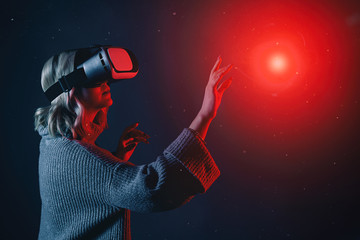 Beautiful young blonde woman wearing a VR glasses touching imaginary object in air during the virtual reality experience