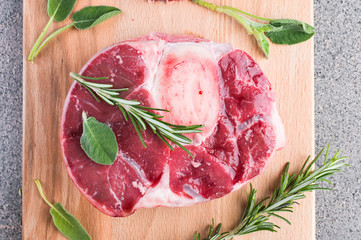 Sliced meat on a wooden board with herbs and spices. Raw meat on the bone close-up. Gray background.