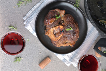 A large piece of fried meat on the bone in a plate and a glass of red wine. Hearty male lunch.