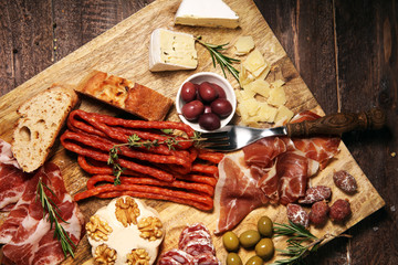 Cutting board with prosciutto, salami, cheese,bread and olives on dark wooden background