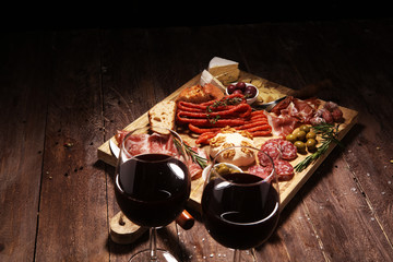Cutting board with prosciutto, salami, cheese,bread and olives on dark wooden background