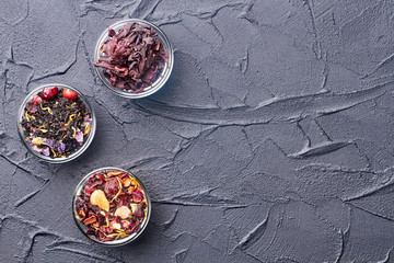 Assortment of dried tea in glass bowls. Aromatic dry tea in transparent bowls on dark stone background with text space.