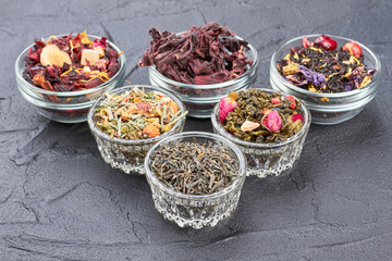 Bowls with different types of dried tea. Collection of transparent bowls with natural tea on black stone.