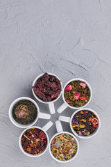 Mix of dry tea in cups and copy space. Ceramic cups with variety of dry tea leaves on gray background. Top view and text space.