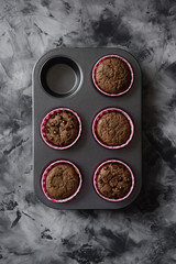 Delicious chocolate muffins in baking tin on dark background top view