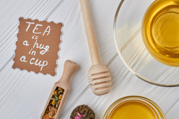 Composition with aromatic healthy tea on wooden background. Herbal tea, honey, dry tea and paper card. Tea is a hug in a cup.